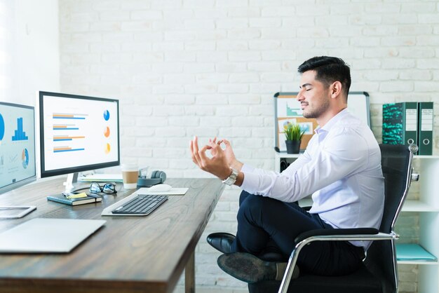 Full length side view of young businessman meditating while sitting on chair at desk