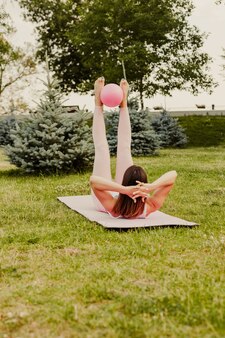 A full-length slender woman in a pink top does exercises for a beautiful abs in the park in the summer, the concept of body care and a slow life.