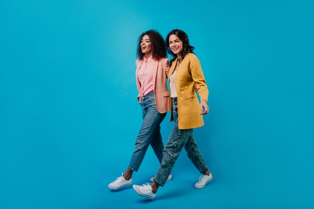 Полнометражный студийный снимок двух модных женщин, идущих по синей стене