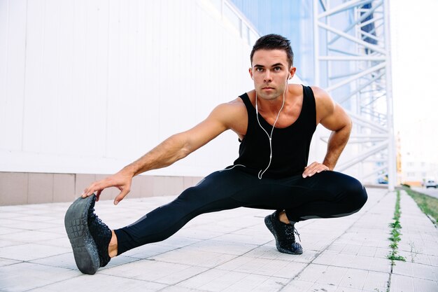 Full length view of athlete male doing stretching exercises for body, listening to music