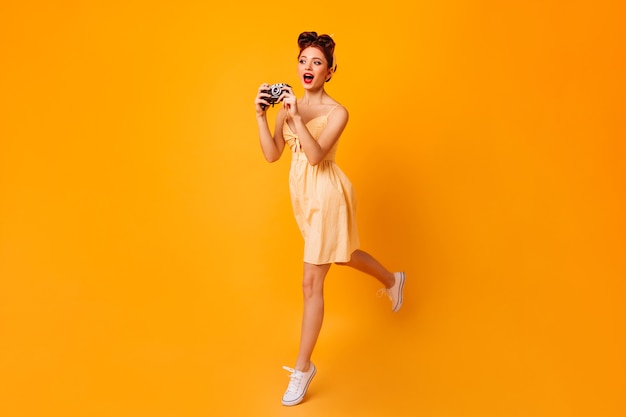 Full length view of dancing photographer. Studio shot of pinup girl jumping with camera.