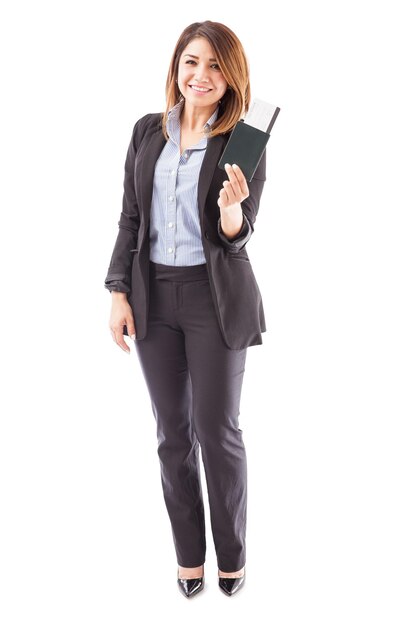Full length view of a female sales executive of an airline holding a boarding pass and a passport on a white background
