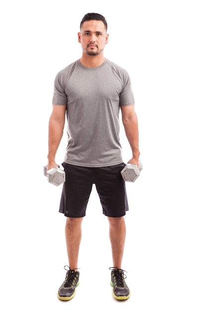 Full length view of a Hispanic strong man lifting a couple of dumbbells on a white background