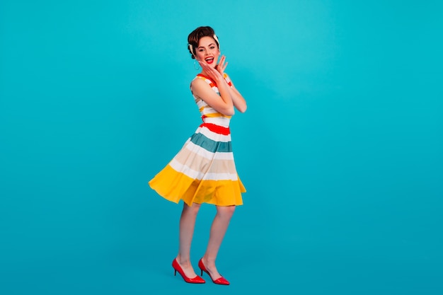 Free photo full length view of pinup girl in striped dress. studio shot of brunette lady dancing on blue background.