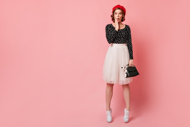 Full length view of surprised girl in white skirt. Studio shot of amazed french lady in elegant beret.