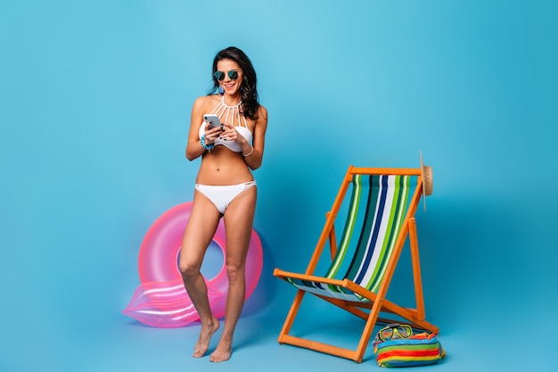 Vista integrale della donna abbronzata in bikini utilizzando smartphone