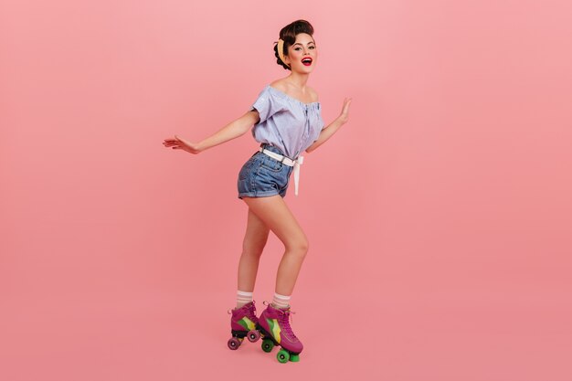 Full length view of woman in roller skates. Studio shot of slim pinup girl in denim shorts.