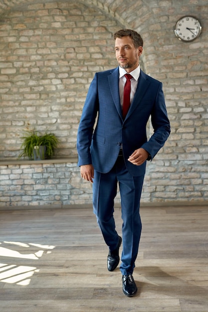 Free photo full length of well dressed businessman walking in the office and looking away