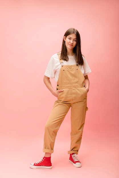 Free photo full length young caucasian brunette woman wears tshirt overalls and running shoes on pink background lifestyle concept