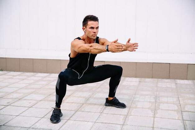 Full length of young concentrated sportsman doing squats during workout outdoors