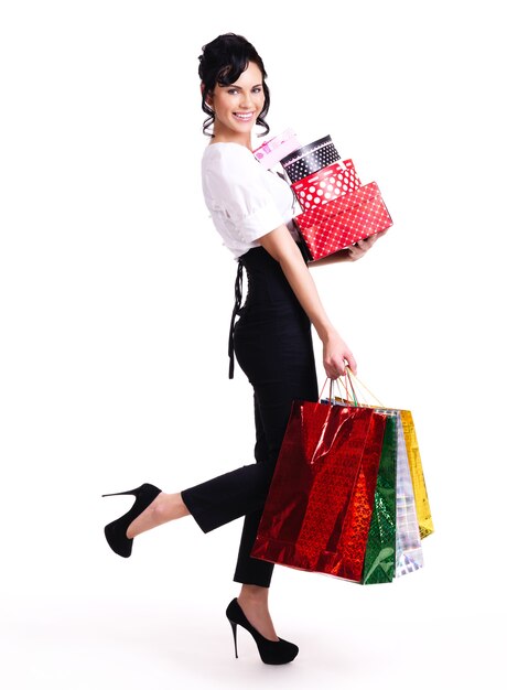 Full portrait of happy woman with color shopping bags and boxes standing isolated on white background.