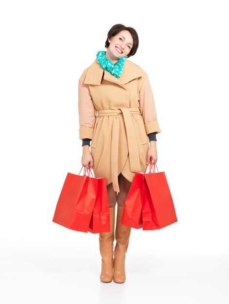 Full portrait of happy woman with shopping bags in autumn coat with green scarf standing isolated on white