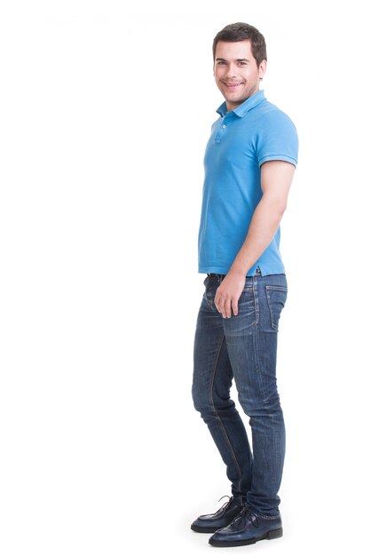 Full portrait of smiling happy handsome man in blue jeans standing isolated on white wall.