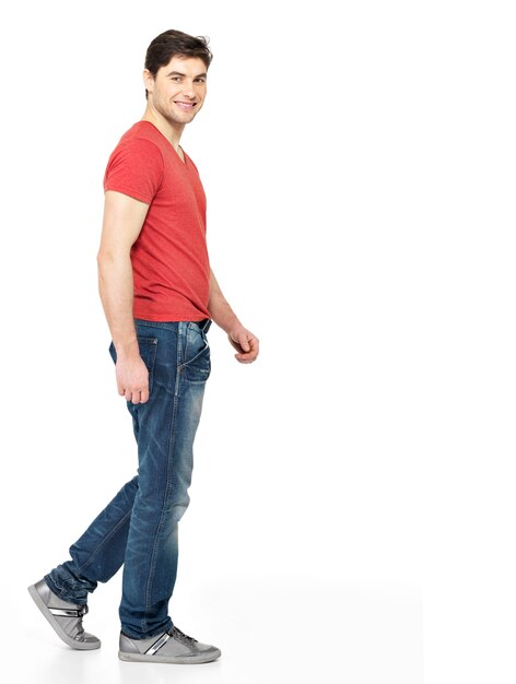 흰색 배경에 고립 된 빨간 티셔츠 캐주얼에 웃는 걷는 남자의 전체 초상화.