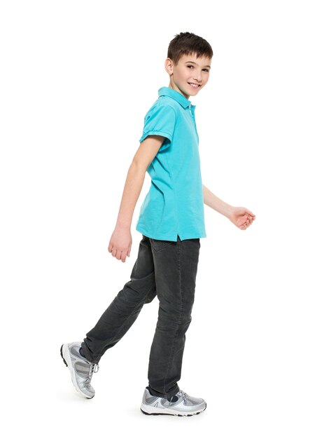 Полный портрет улыбающегося идущего мальчика-подростка в синей футболке вскользь, изолированных на белом.