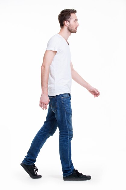 Полный портрет идущего человека в белой футболке вскользь - изолированный на белизне.
