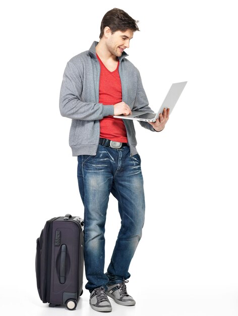 Full portrait of young smiling happy man with suitcase and laptop isolated on white