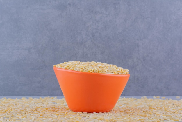 Full rice bowl sitting on a scattered mass of brown rice on marble surface