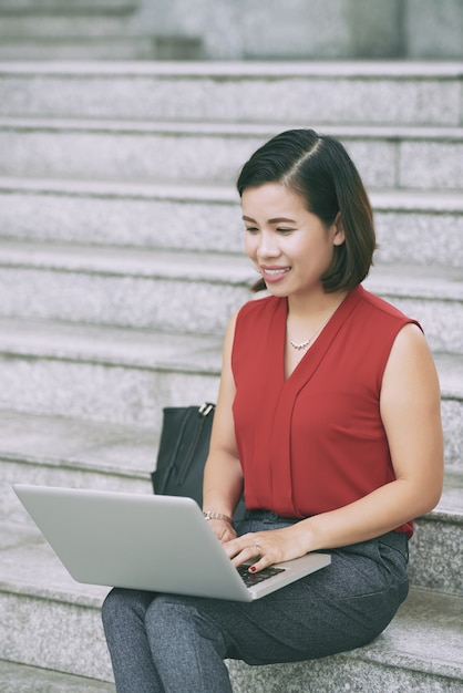 Foto gratuita colpo completo della donna attraente che per mezzo del computer portatile messo sulle scale all'aperto