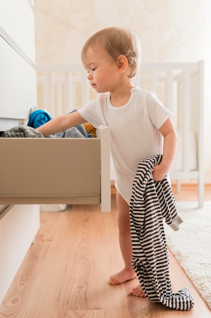 フルショットの赤ちゃんが引き出しから服を着て