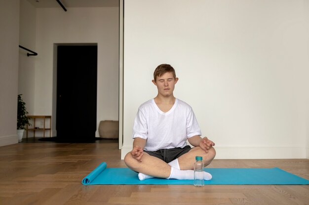 Мальчик в полный рост медитирует на коврике для йоги