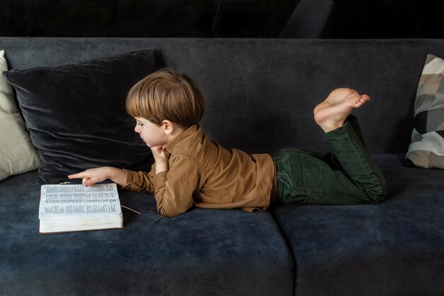 Full shot boy reading bible on couch