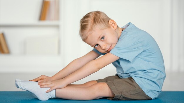 マットの上でストレッチフルショットの少年