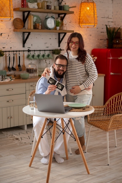 Foto gratuita coppia a figura intera che annuncia la gravidanza con il laptop