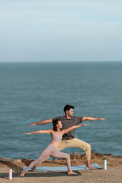 Free photo full shot couple doing yoga together on beach