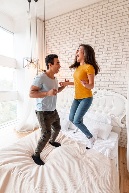 Full shot couple jumping in the bed