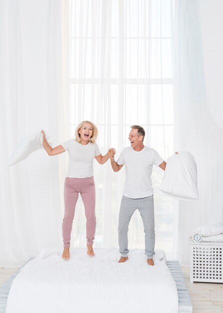 Full shot couple jumping in the bed