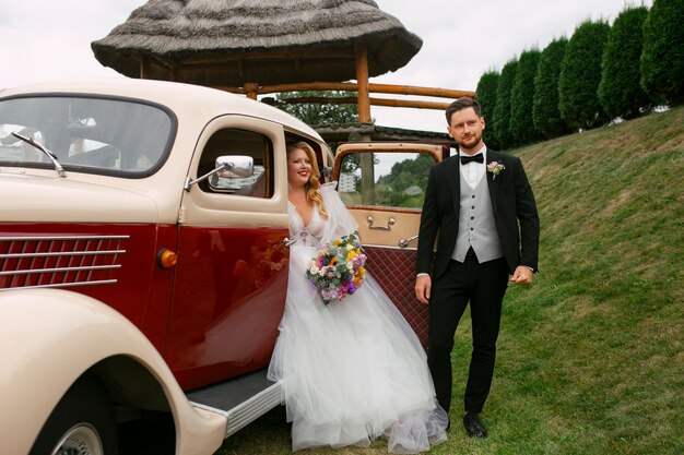 Full shot couple posing with vintage car