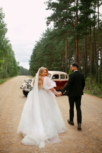 Full shot couple posing with vintage car