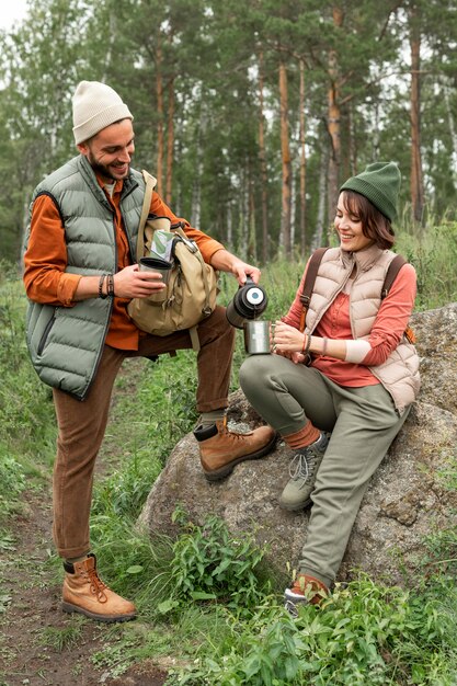 Full shot couple pouring hot drink in nature