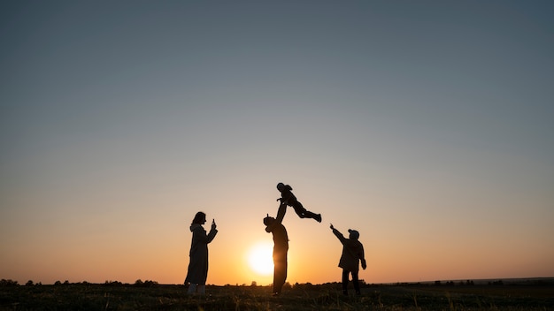 Foto gratuita siluetta della famiglia del colpo pieno che si diverte al tramonto