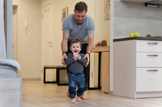 Full shot father helping kid walk at home