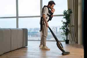 Free photo full shot father holding baby while vacuuming