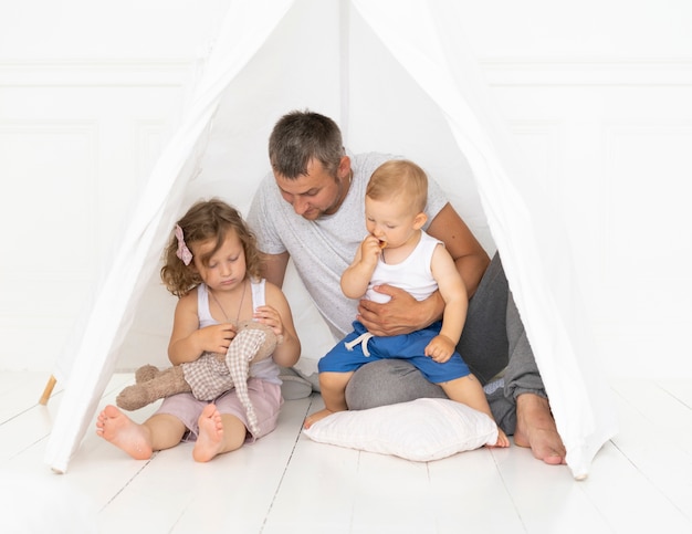 Full shot father playing with his kid in a tent