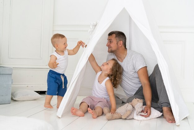 Full shot father playing with kids with tent