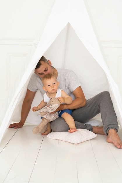 Free photo full shot father sitting with baby boy under tent