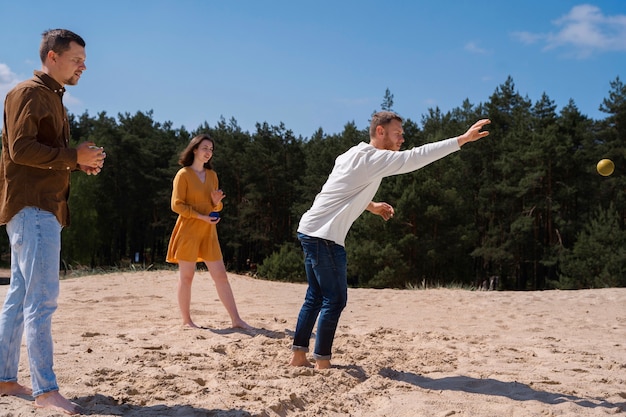 Free photo full shot friends playing pétanque at beach