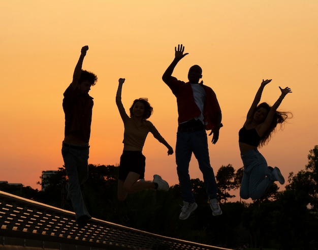 Бесплатное фото Силуэты друзей в полный рост, прыгающие на закате
