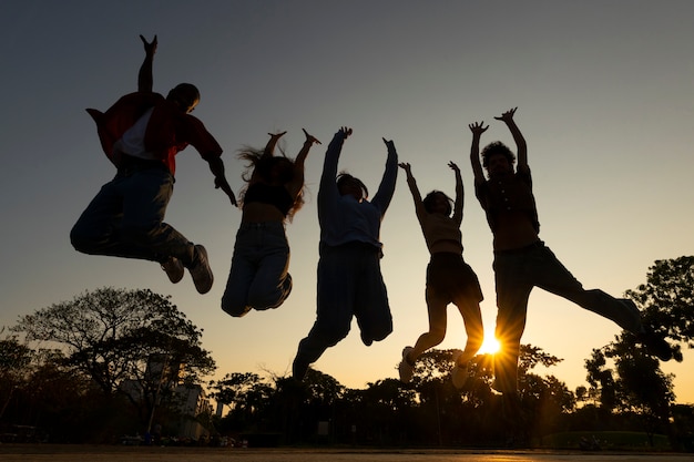 Free photo full shot friends silhouettes jumping at sunset