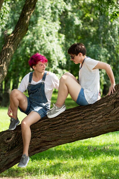 Free photo full shot friends sitting on tree trunk