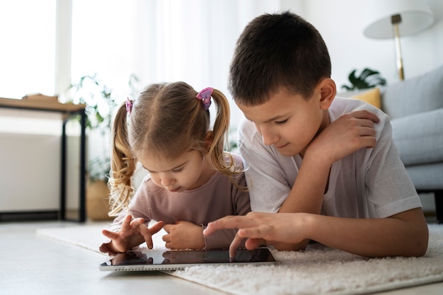 Free photo full shot girl and boy with tablet at home