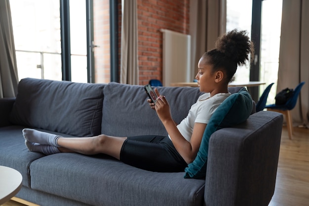Full shot girl on couch with smartphone