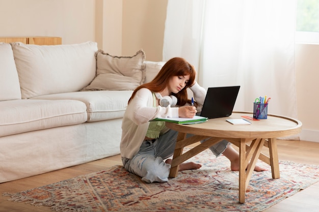 Foto gratuita ragazza a tutto campo che impara con il laptop sul pavimento