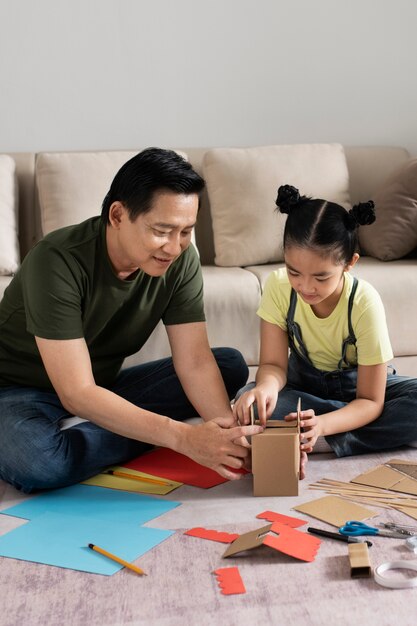 Full shot girl and man making paper house