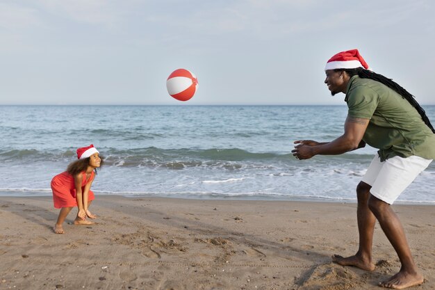 Ragazza e uomo del colpo pieno che giocano con la palla sulla spiaggia