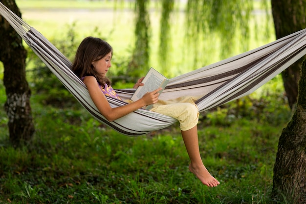 Free photo full shot girl reading in hammock